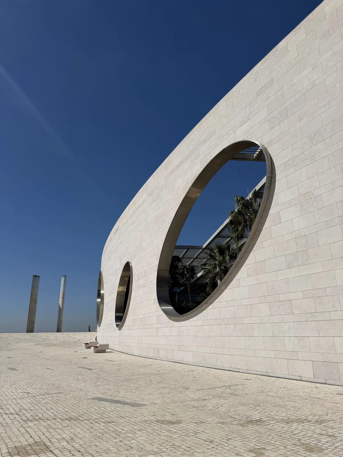 Parede branca e curva com janelas redondas enormes, contra um céu azul escuro.