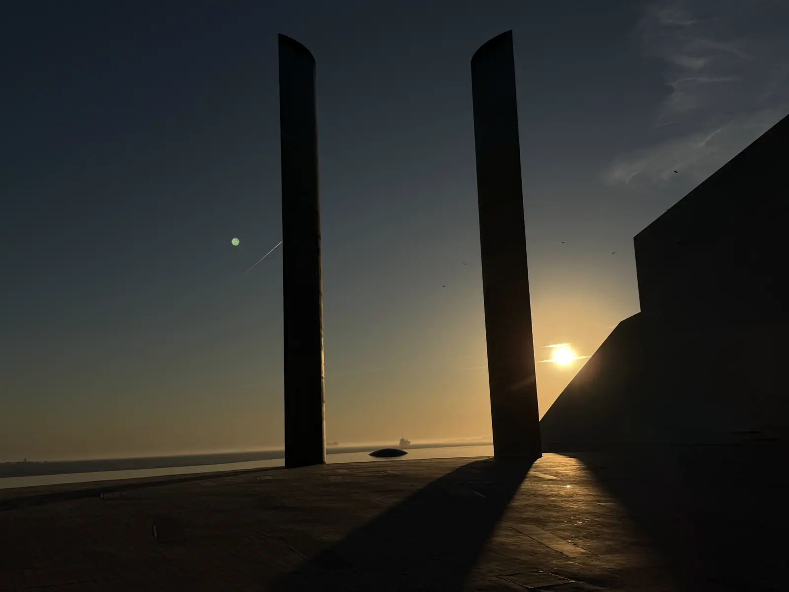 Dois monólitos altos em silhueta contra o sol que se põe sobre o rio.