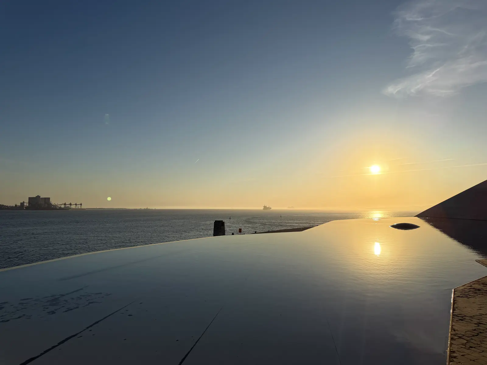 Pôr do sol sobre o rio, refletido no espelho d'água, com a borda escura do prédio à direita.