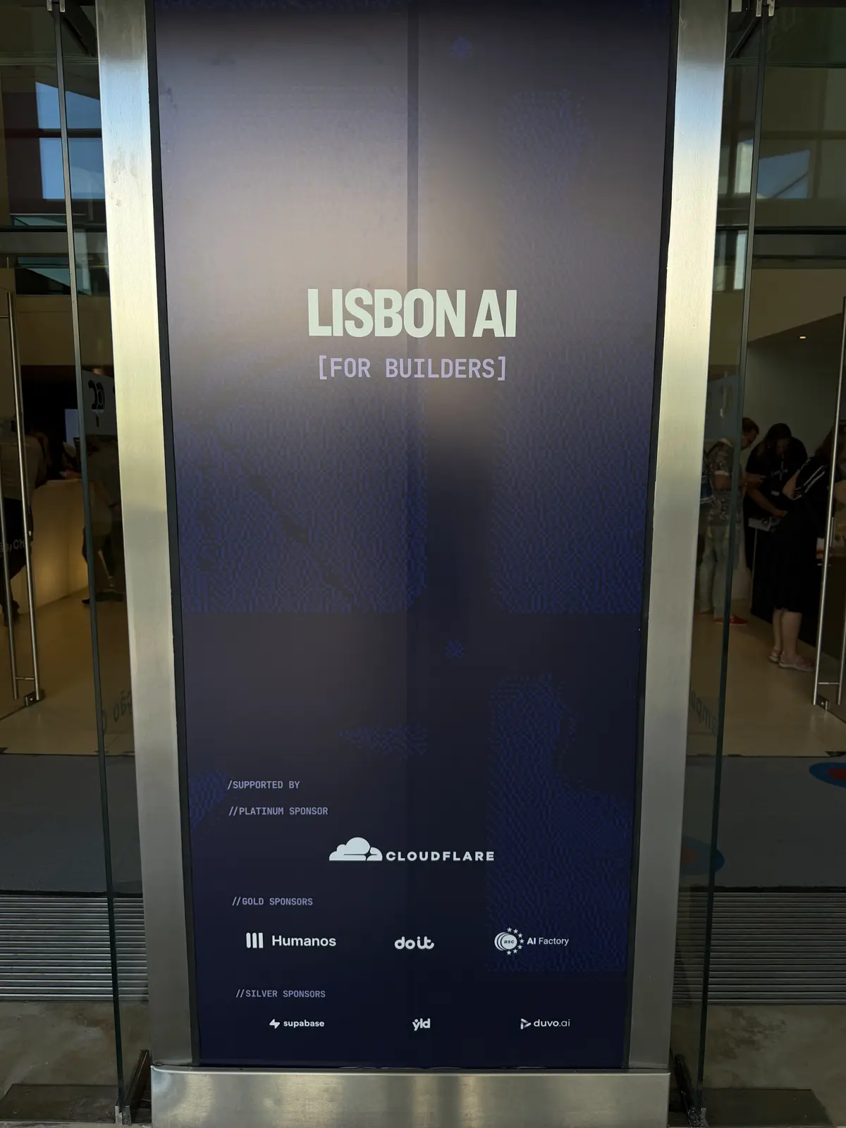 Totem escuro na entrada com o texto LISBON AI [for builders] e logos de patrocinadores.